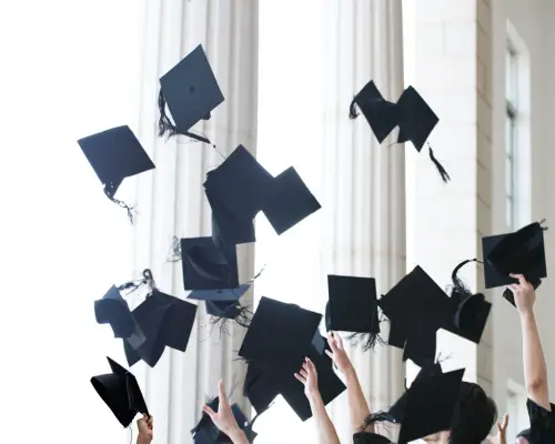 Graduation caps being thrown in the air in front of a university building, symbolizing academic achievement